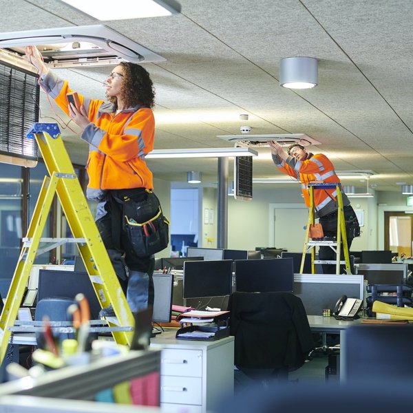 Two trades people install commercial air conditioning units in an office