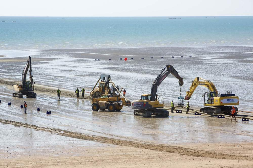 Excavators on the beach lift the Normandie 3 subsea cable into place.