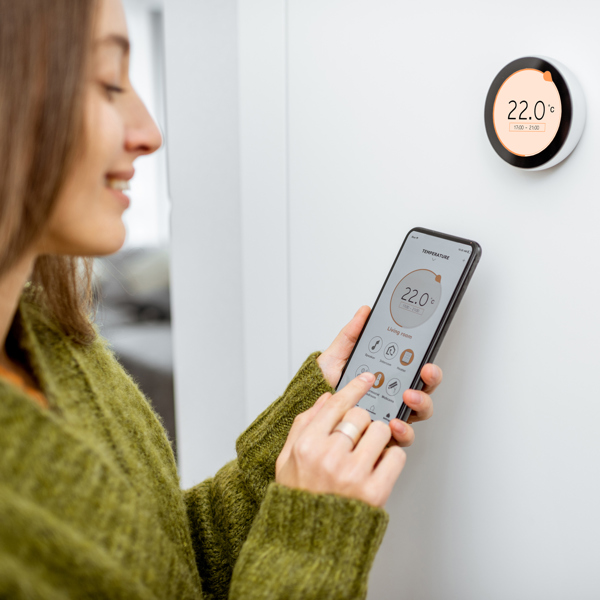 A young woman uses her phone to control her smart heating system.