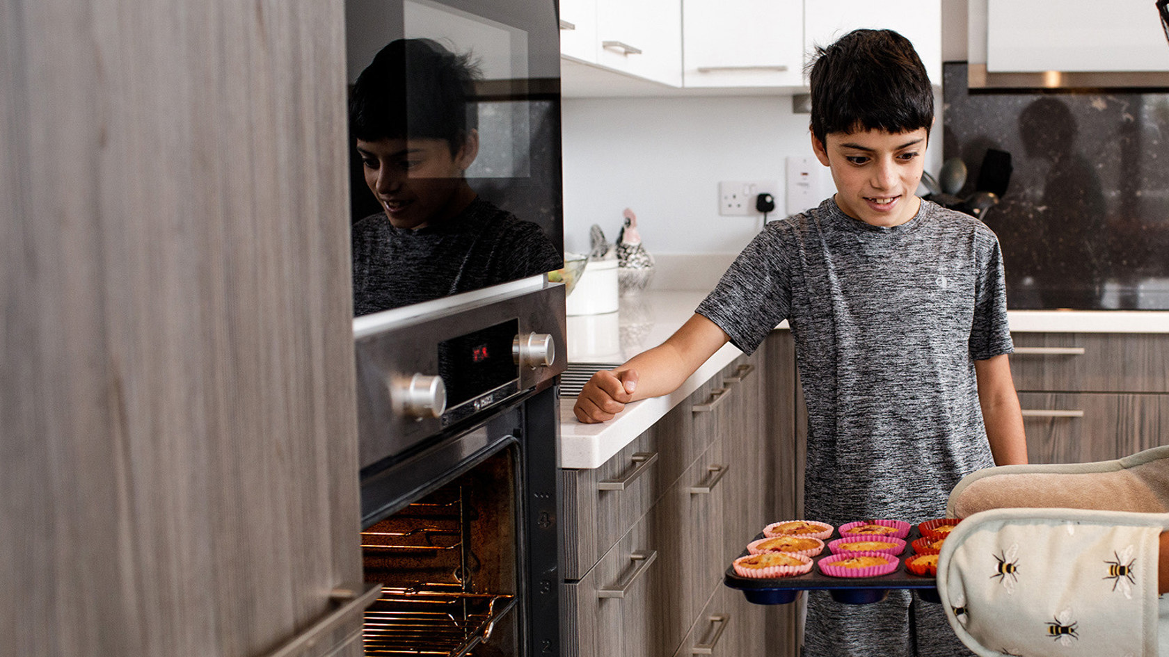 A mother removes her cupcakes from her electric oven as her son looks on.