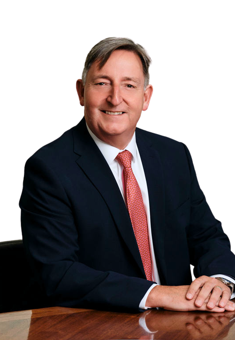 Paul Savery wearing a dark suit and red tie seated at a table. The background is white