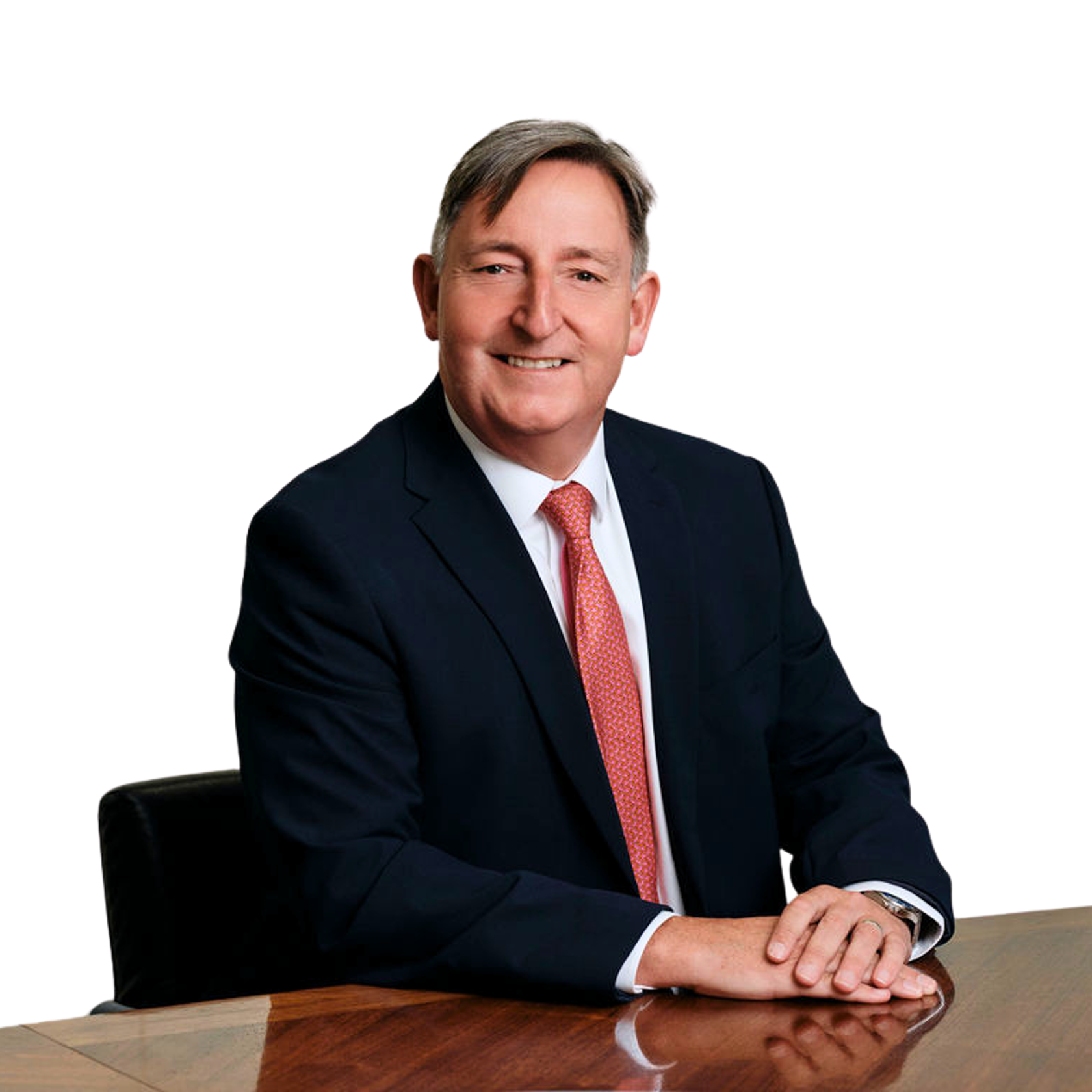 Paul Savery wearing a dark suit and red tie seated at a table. The background is white