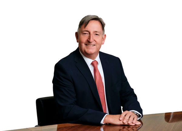 Paul Savery wearing a dark suit and red tie seated at a table. The background is white