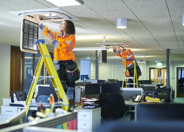 Two trades people install commercial air conditioning units in an office