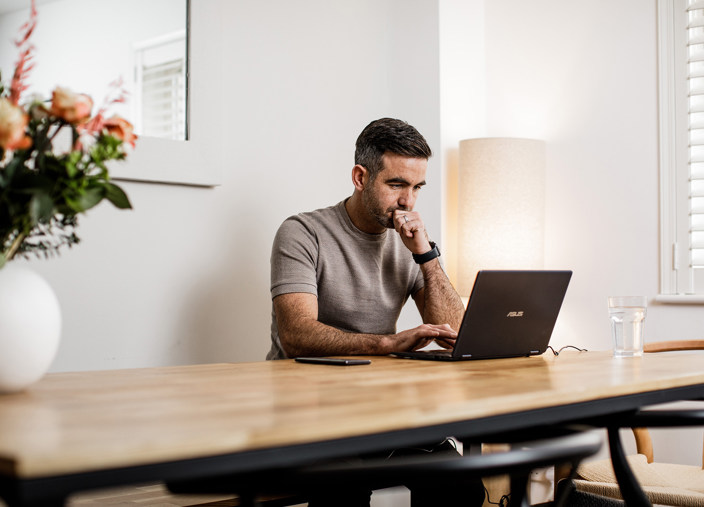 Man searches on a laptop whilst sat at the kitchen table.