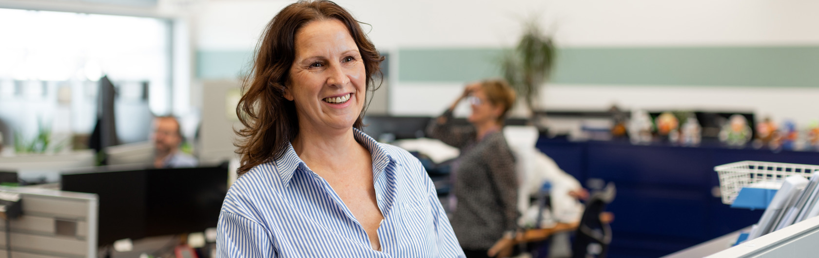 A person smiling and wearing a blue blouse stands at a table looking at finance reports