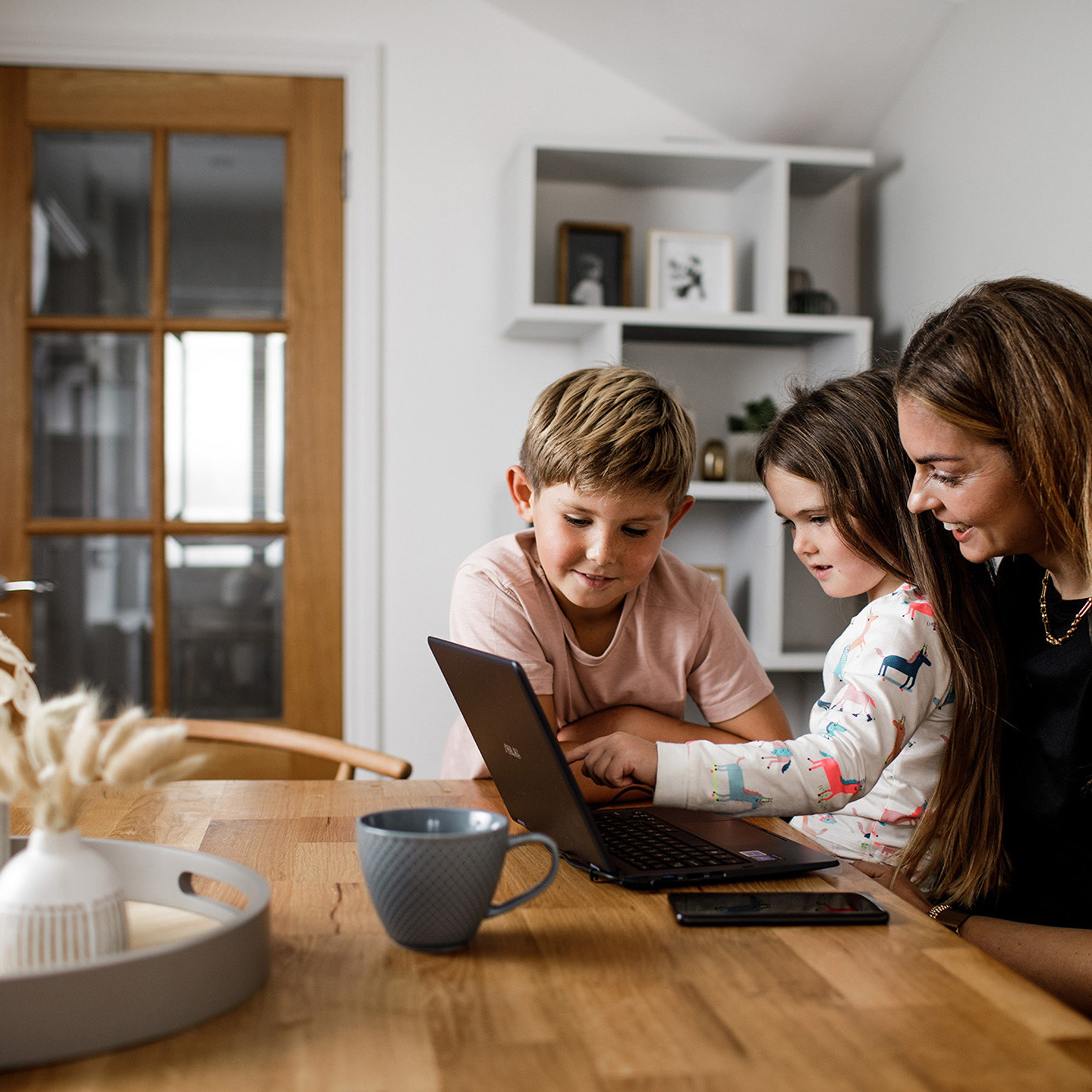 A mother and her children sat at the kitchen table enjoying something on a laptop computer.