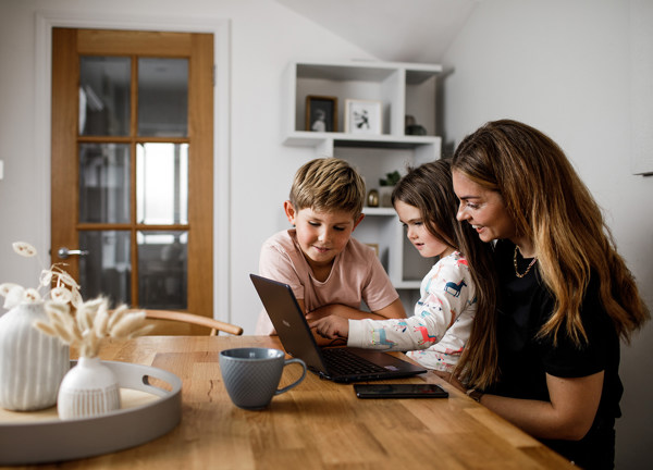 A mother and her children sat at the kitchen table enjoying something on a laptop computer.