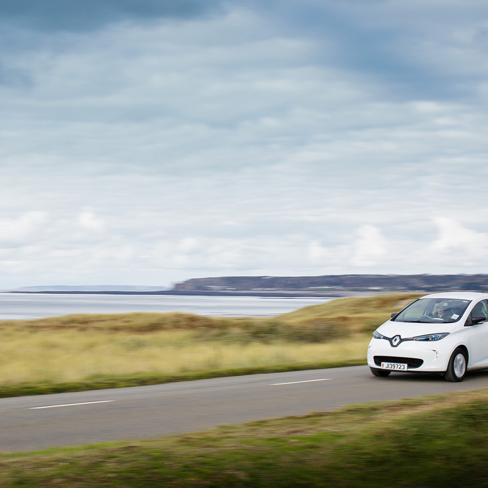 An electric vehicle speeds across the Five Mile Road in St Ouen on a cloudy covered day.