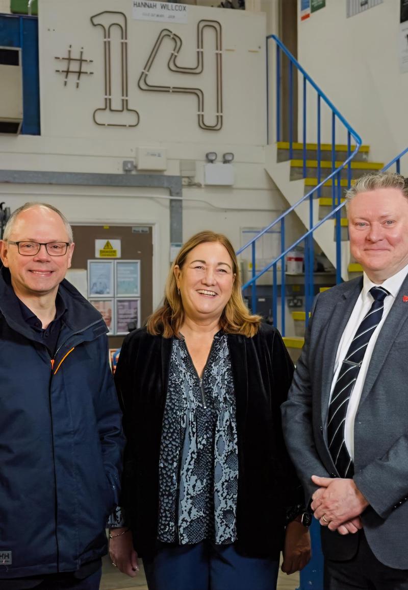 Three people looking at the camera, smiling and standing in a workshop