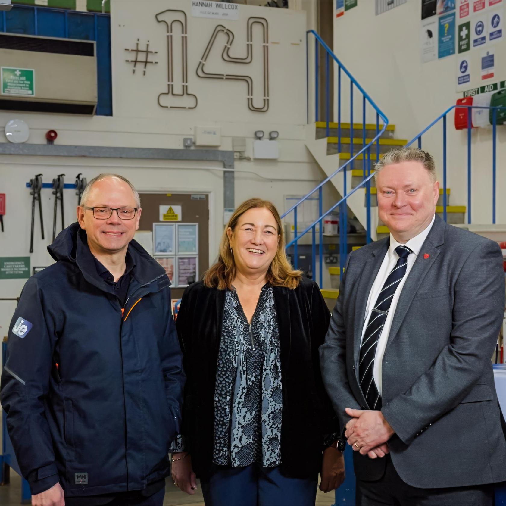 Three people looking at the camera, smiling and standing in a workshop