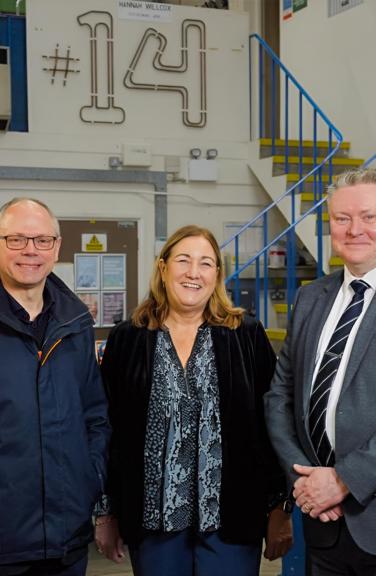 Three people looking at the camera, smiling and standing in a workshop