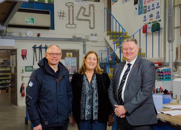 Three people looking at the camera, smiling and standing in a workshop