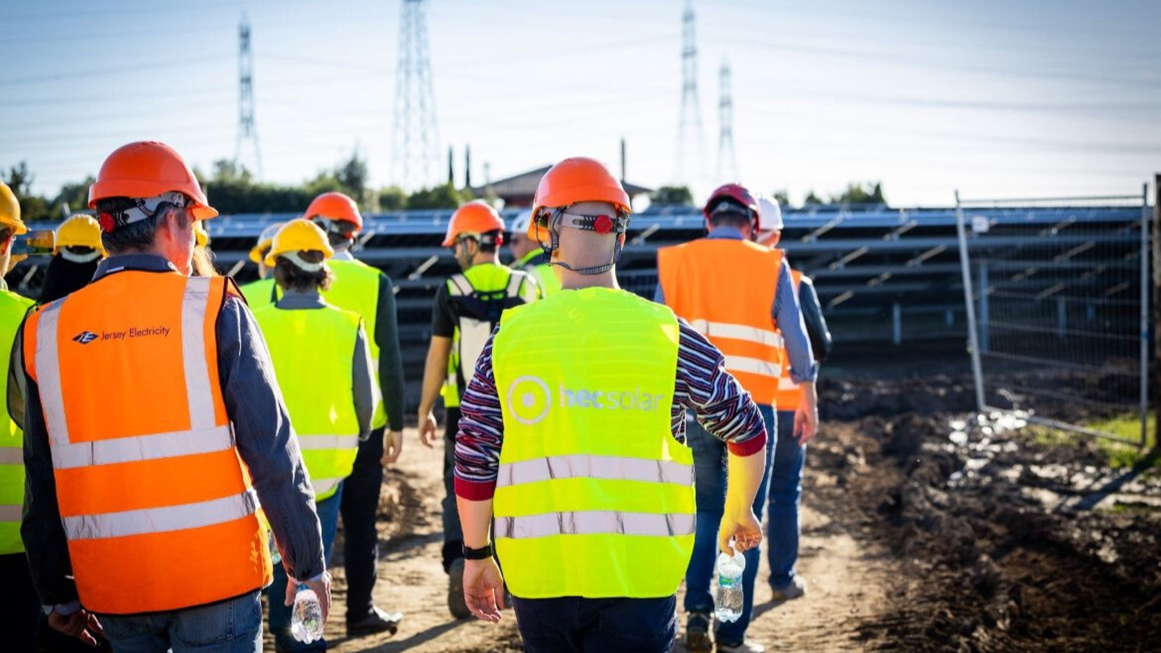 A group of people in high vis jackets walking through a field with solar panels. 
