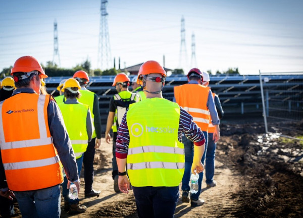 A group of people in high vis jackets walking through a field with solar panels.