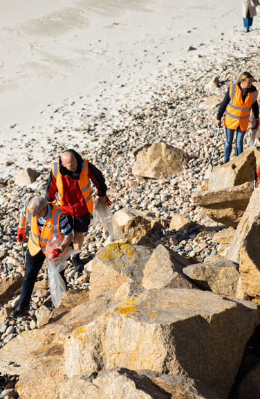 A group of people wearing high vis jackets on a sunny beach, litter picking