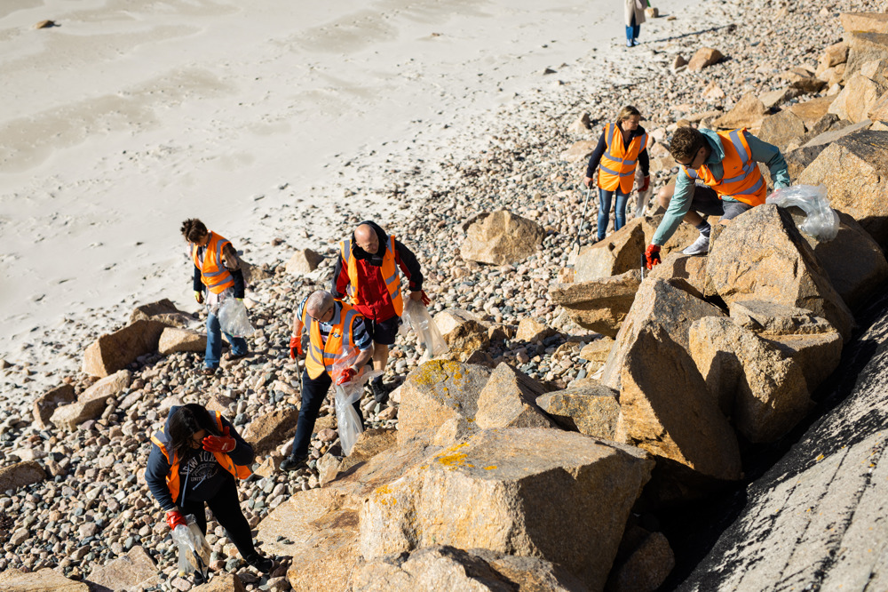 A group of people wearing high vis jackets on a sunny beach, litter picking