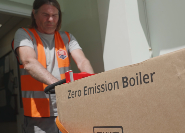 A person in a high vis moving a box through a doorway, the box reads Zero Emisson Boiler