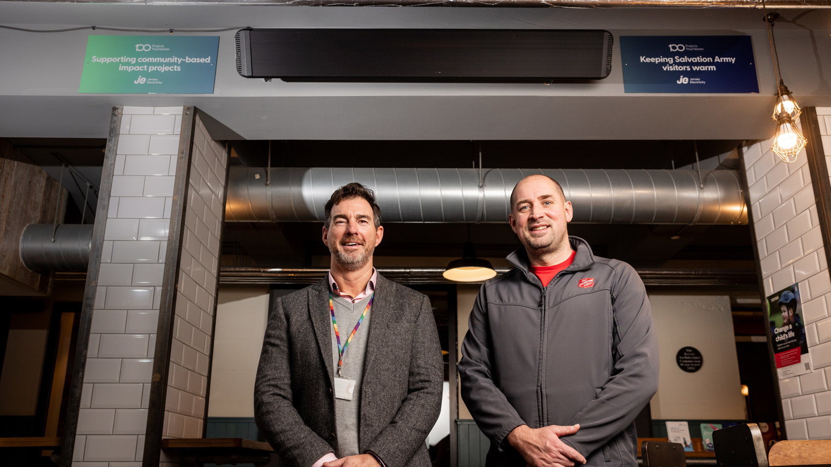 Two people stood in a cafe, smiling with their arms placed in front of them