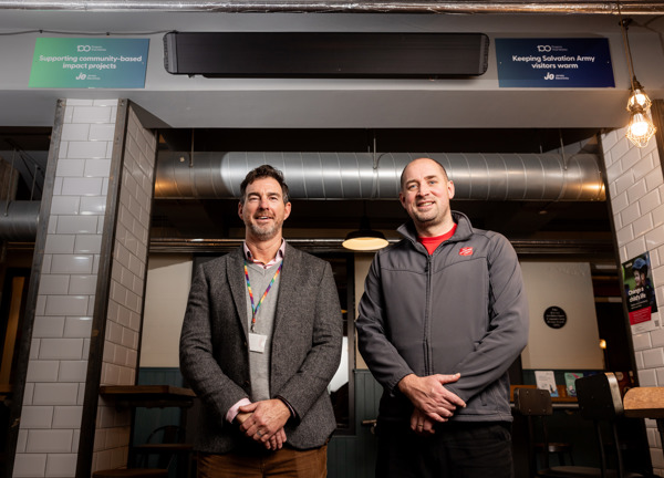 Two people stood in a cafe, smiling with their arms placed in front of them