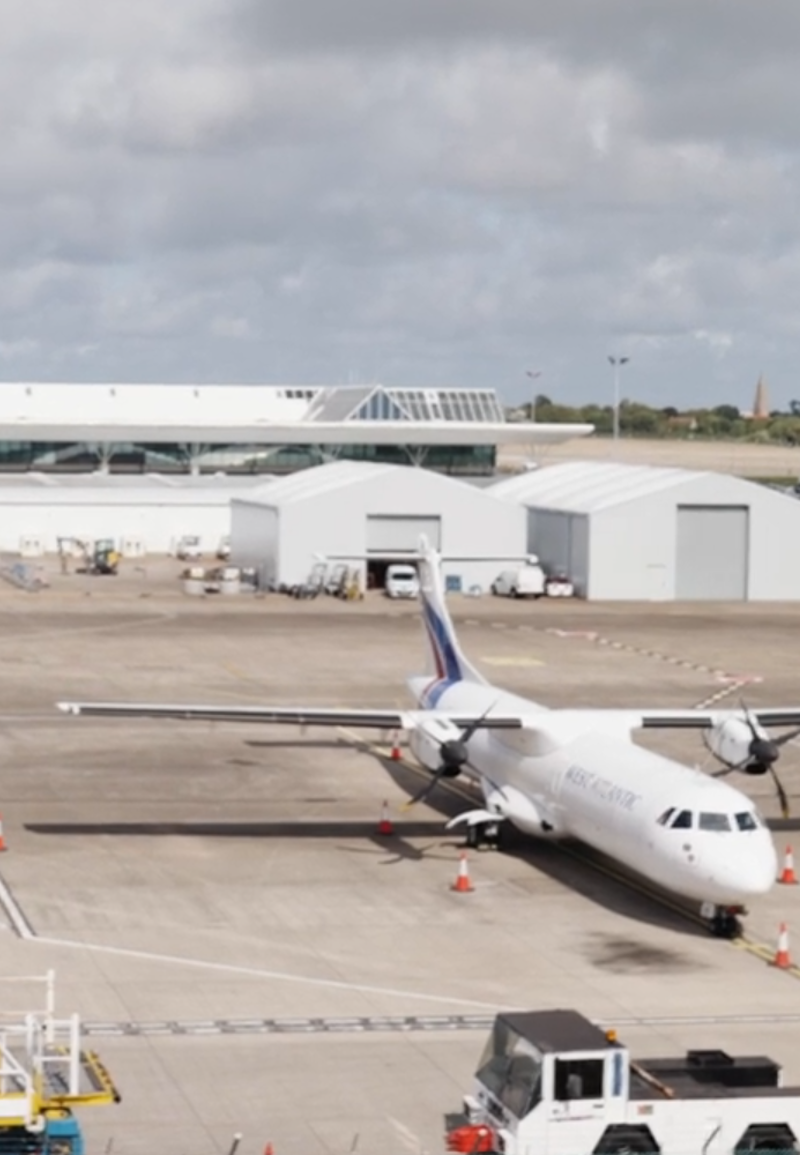 A white passenger plane on the stand with the Jersey airport buildings behind. 