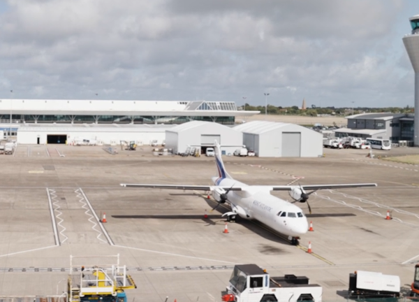 A white passenger plane on the stand with the Jersey airport buildings behind.