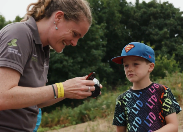 A person in a grey t-shirt looking at wildlife whilst smiling, a small child in a blue cap stands beside them