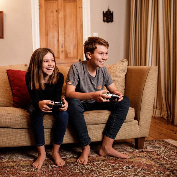 A brother and sister sit on the sofa and play video games.