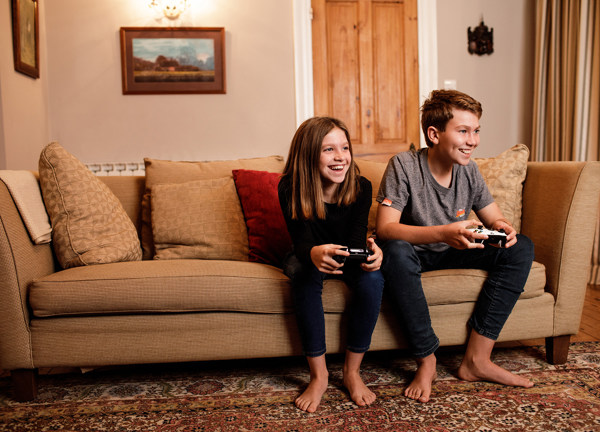 A brother and sister sit on the sofa and play video games.