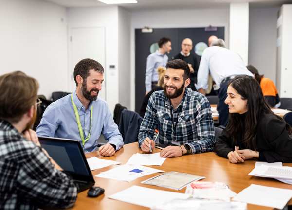 A group of people sat around an office table, smiling whislt looking at competition entries