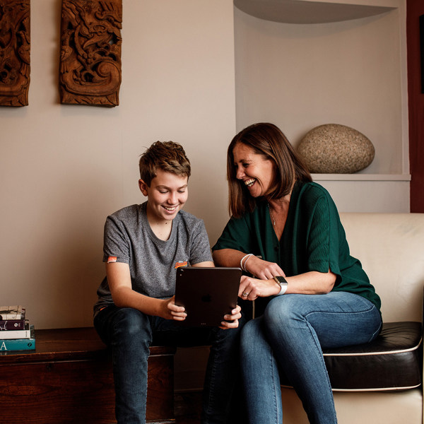 A mother and son laugh together over something they've seen on a tablet.