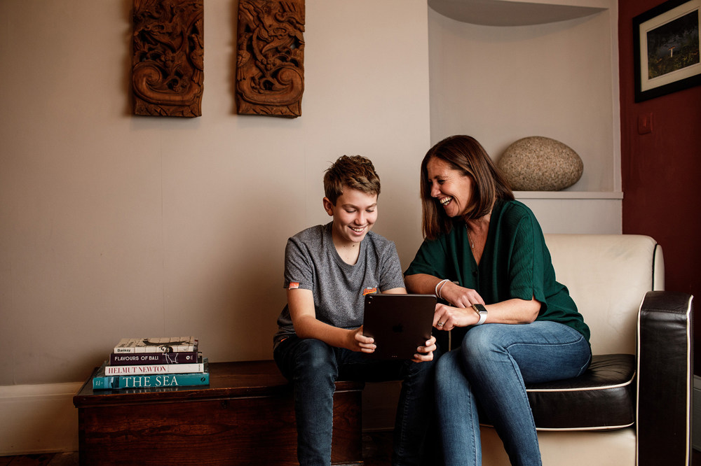 A mother and son laugh together over something they've seen on a tablet.