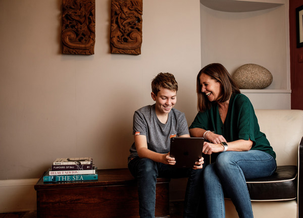 A mother and son laugh together over something they've seen on a tablet.
