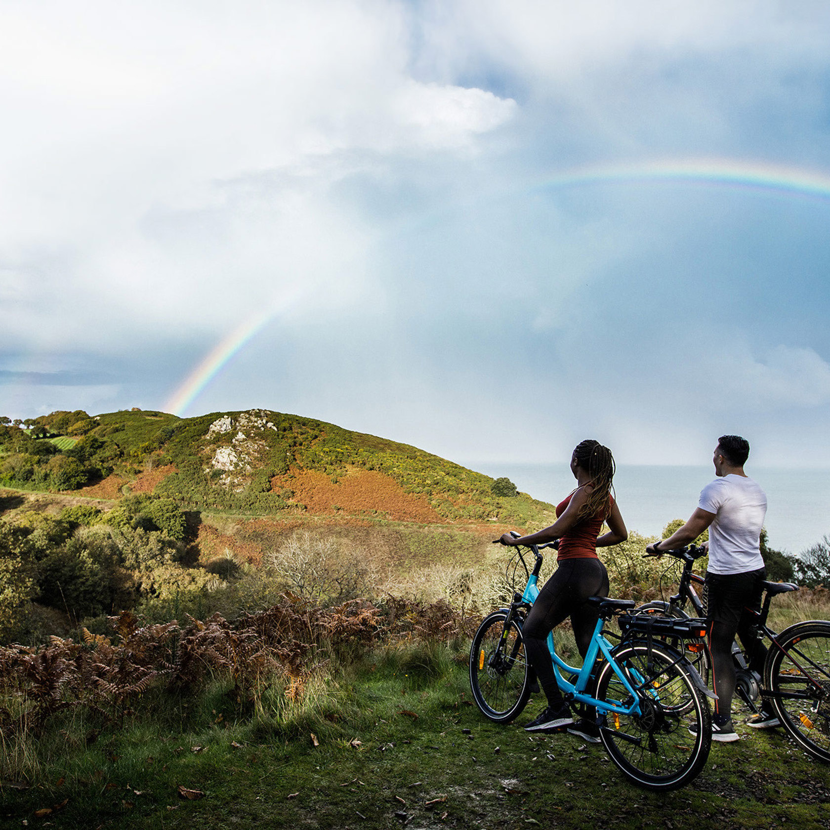 Couple on electric bikes look at rainbow in the countryside