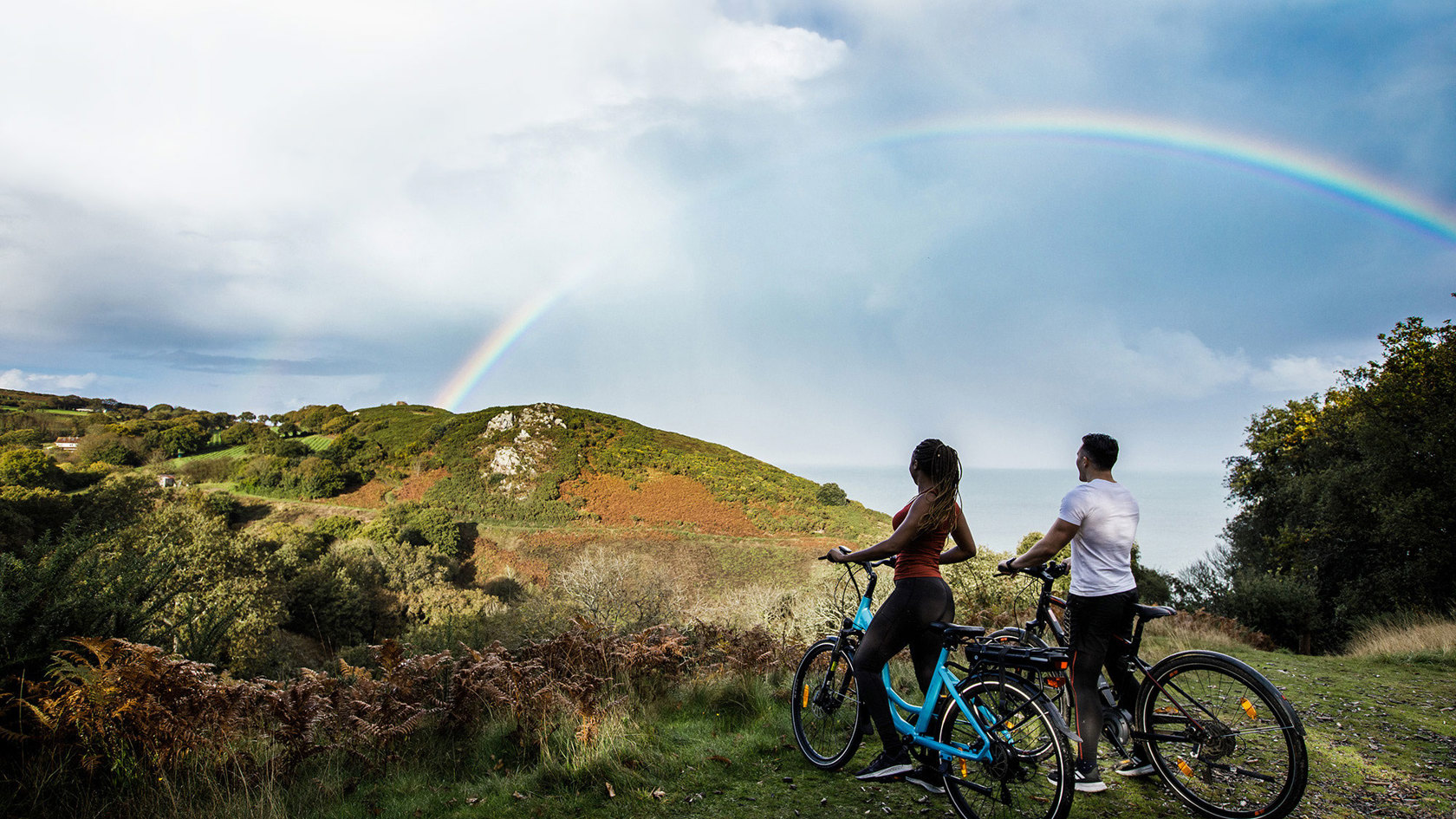 Couple on electric bikes look at rainbow in the countryside