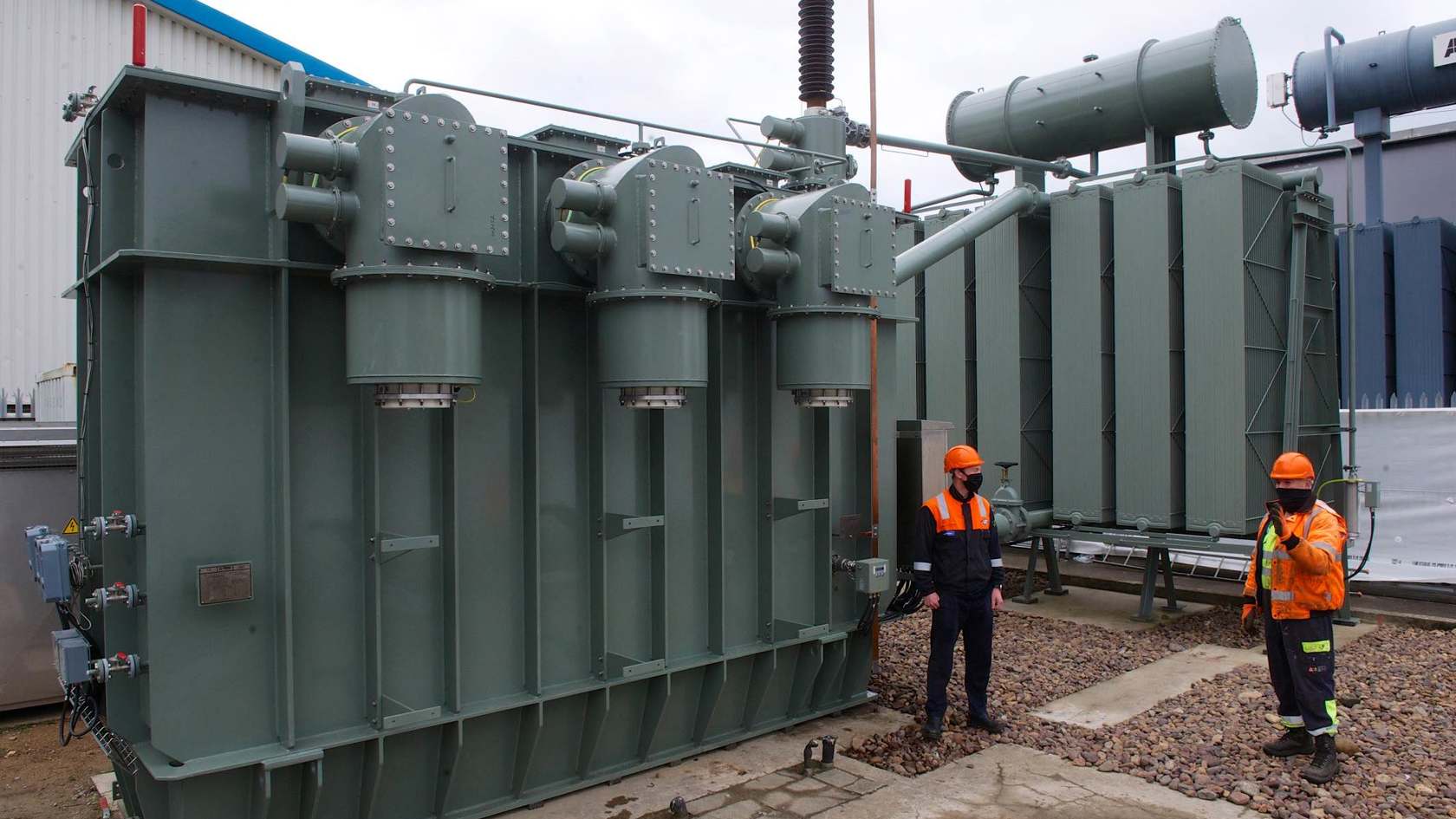Two workers examine a large electricity transformer