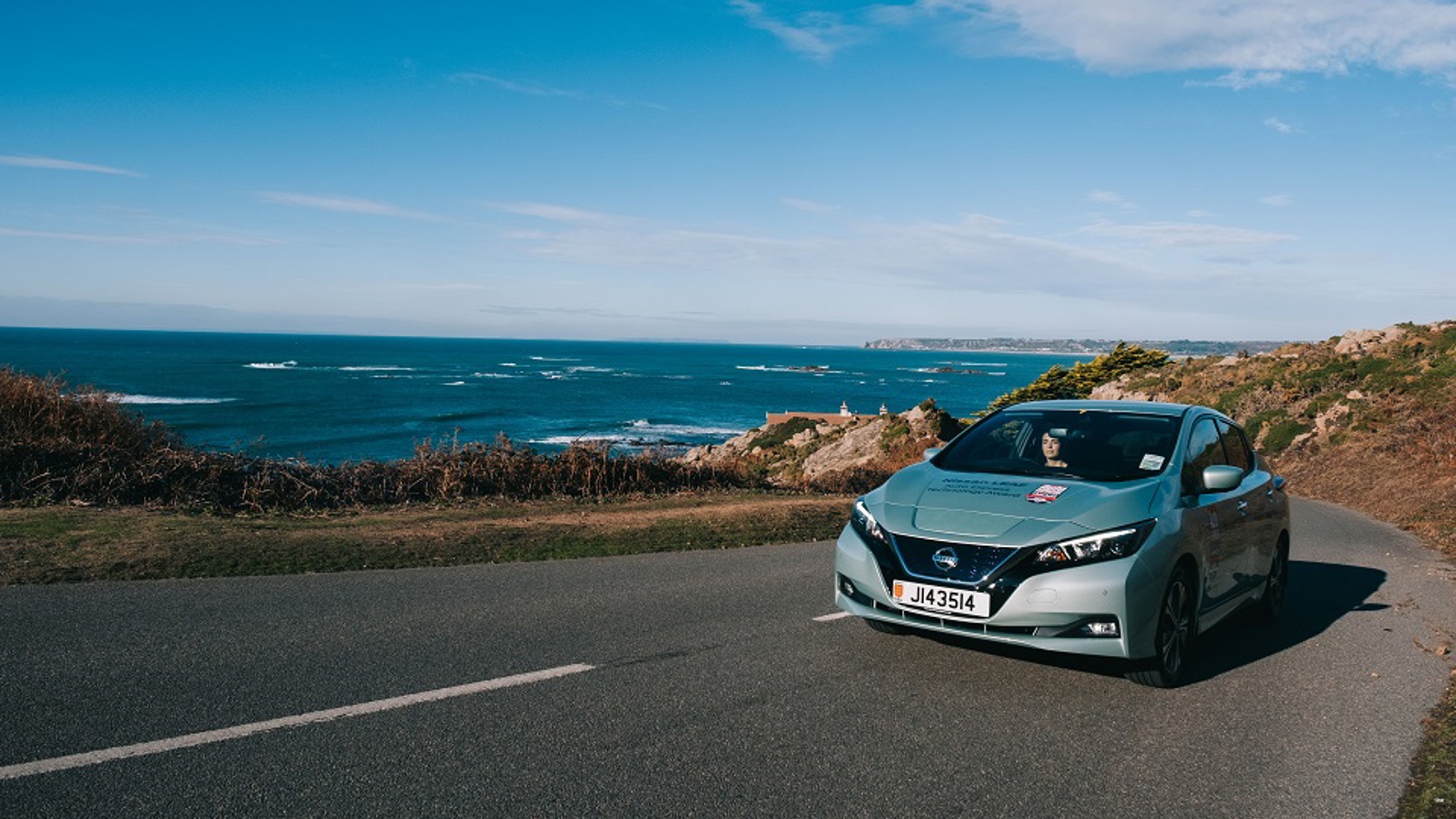 Nissan Leaf driving up a hill with sea behind