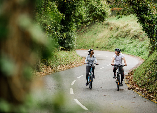 A man and a women cycle electric bicycles through Jersey's country lanes