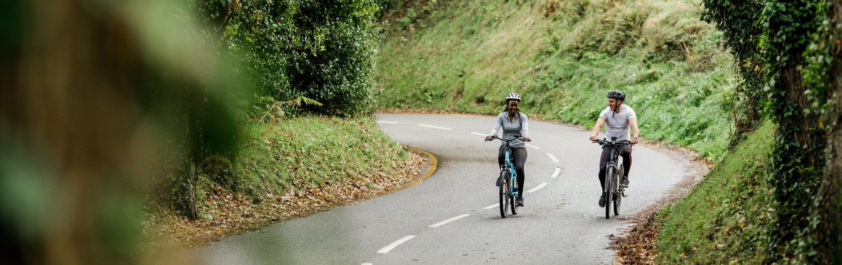 Two people ride electric bikes on quiet country road