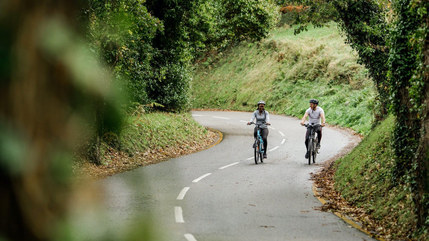 Two people ride electric bikes on quiet country road
