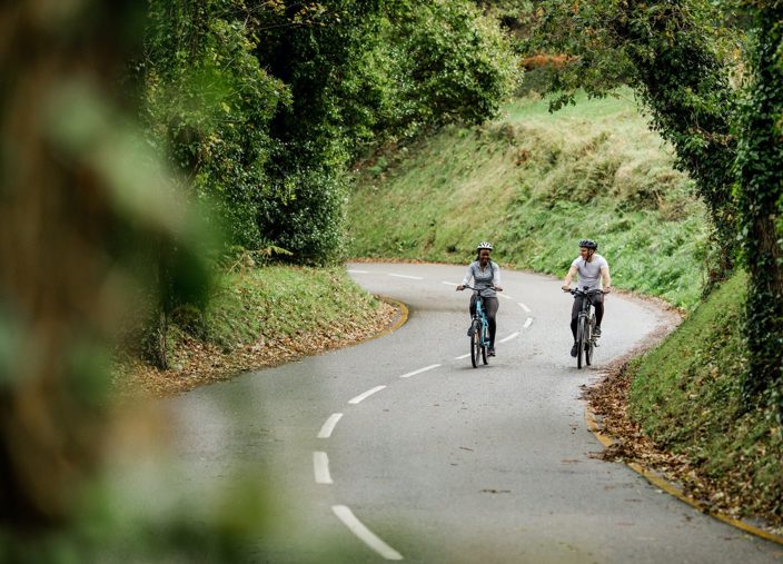Two people ride electric bikes on quiet country road