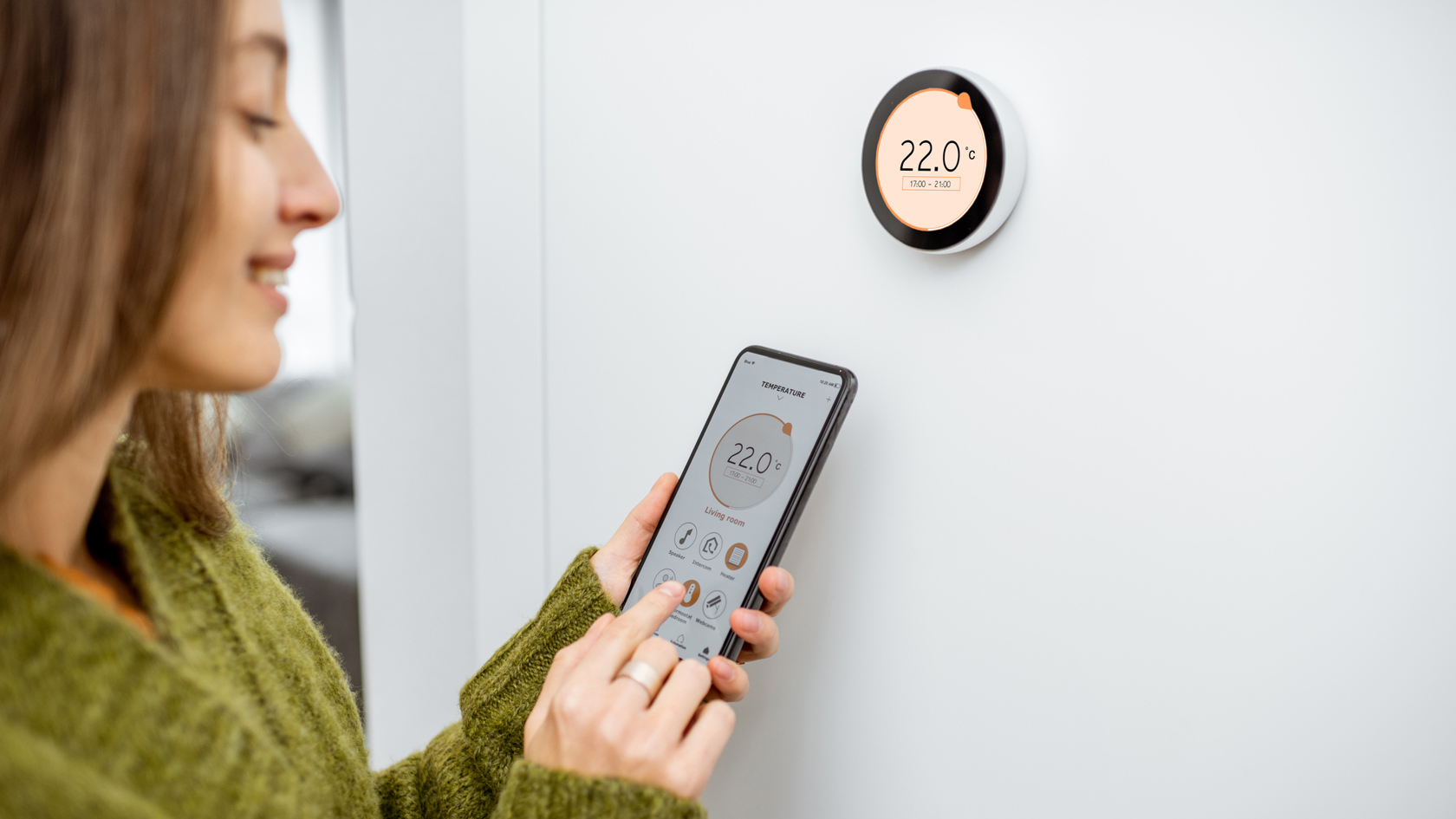 A young woman uses her phone to control her smart heating system.
