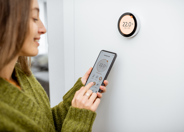 A young woman uses her phone to control her smart heating system.