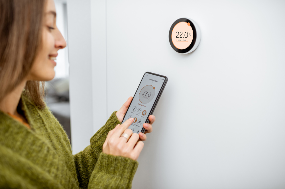 A young woman uses her phone to control her smart heating system.