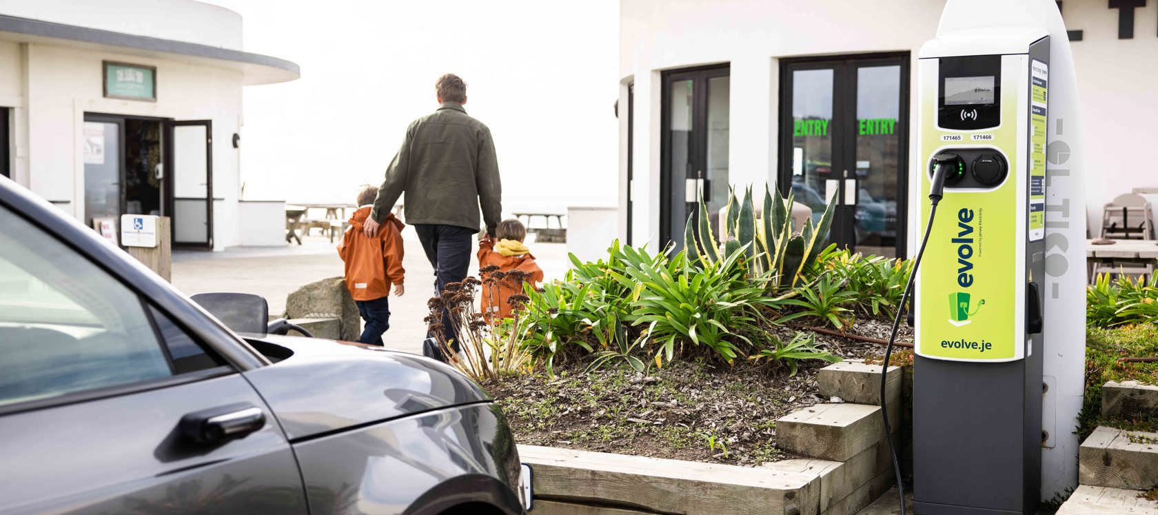 Grey car plugged into Evolve EV charger at El Tico with father and his small boys walking off in the distance.