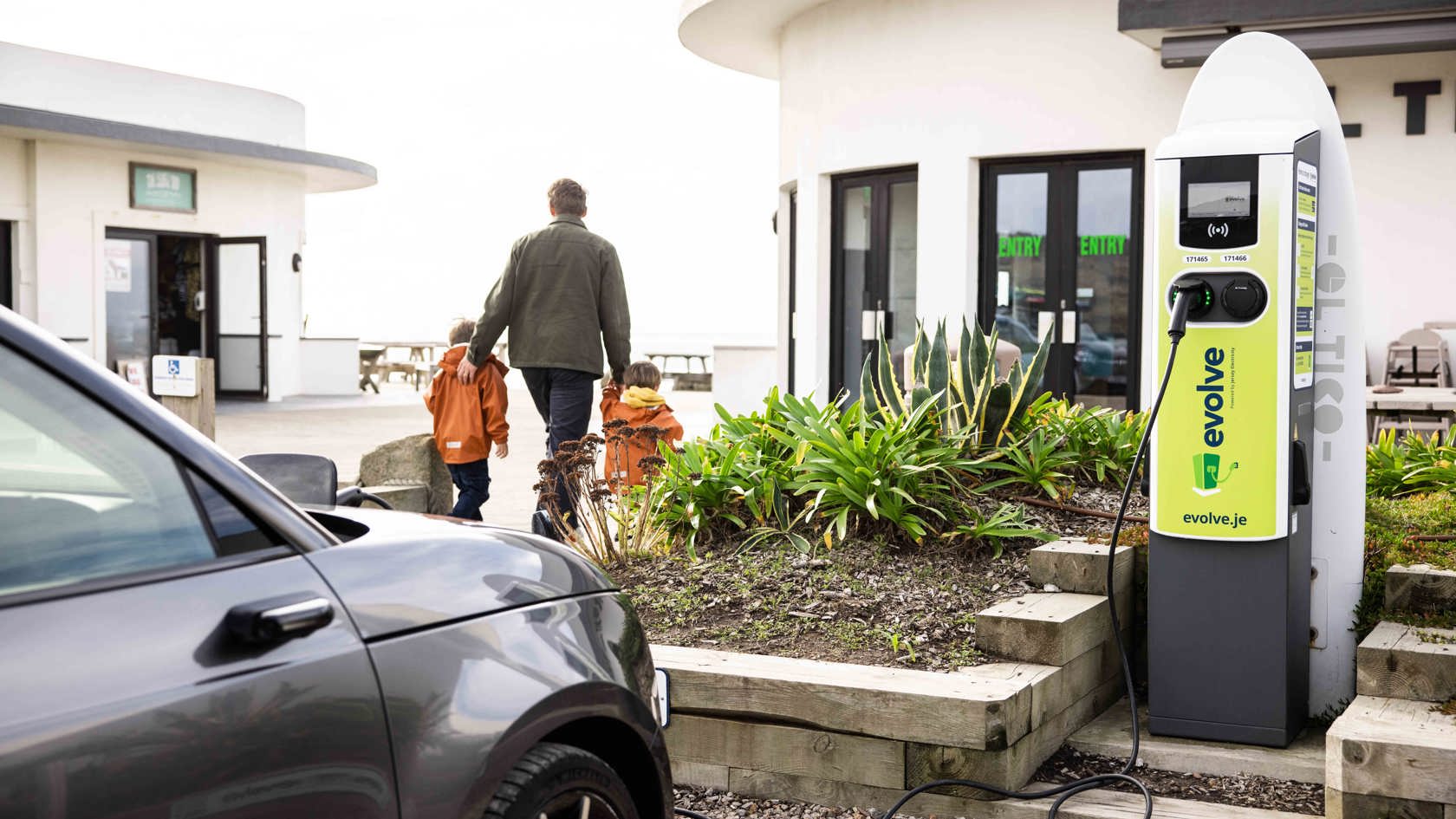 Grey car plugged into Evolve EV charger at El Tico with father and his small boys walking off in the distance.