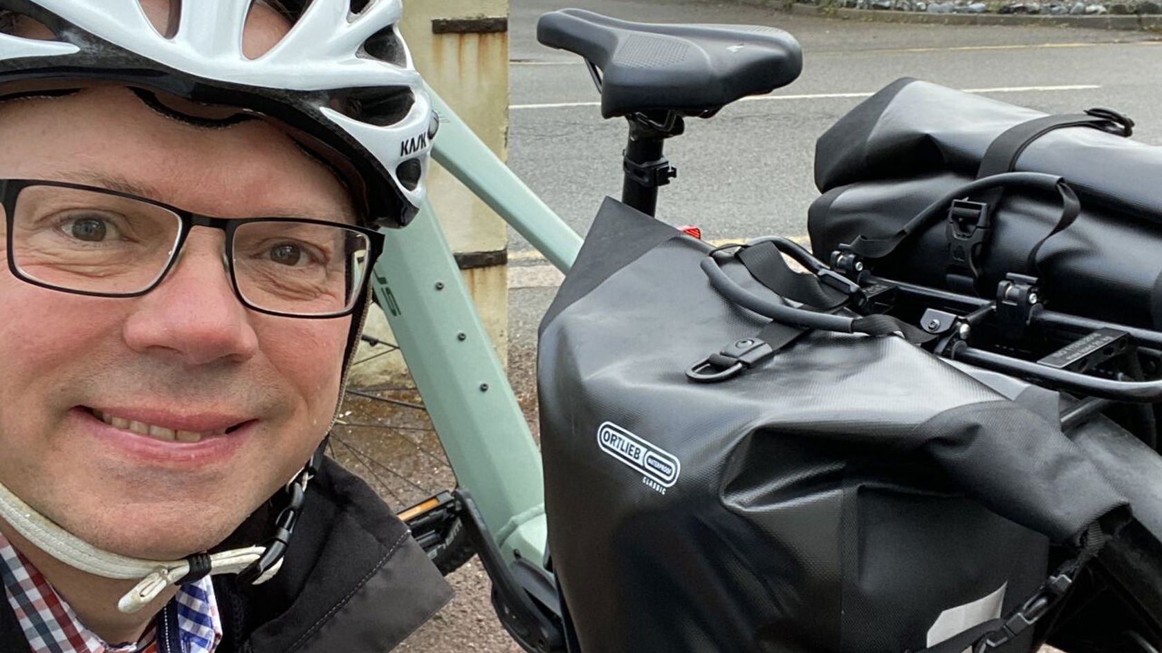 Chris Ambler, Jersey Electricity CEO, wearing a bicycle helmet and kneeling next to his electric bike