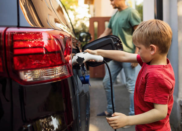 Child in red shirt plugs an electric vehicle charger into a car