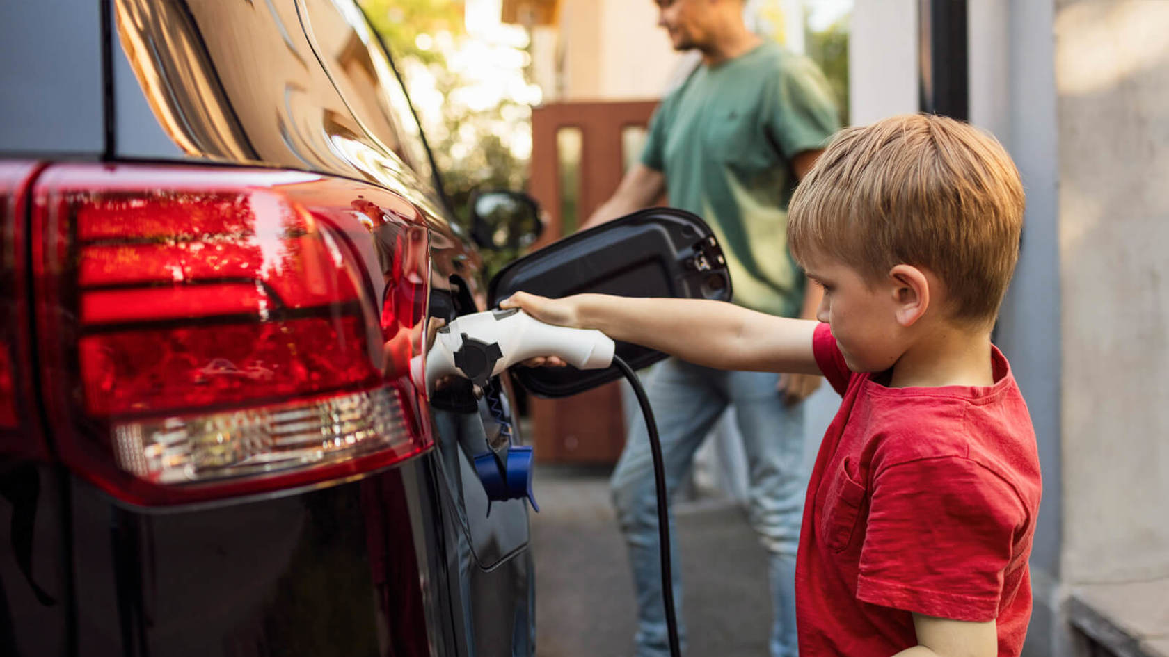 Child in red shirt plugs an electric vehicle charger into a car