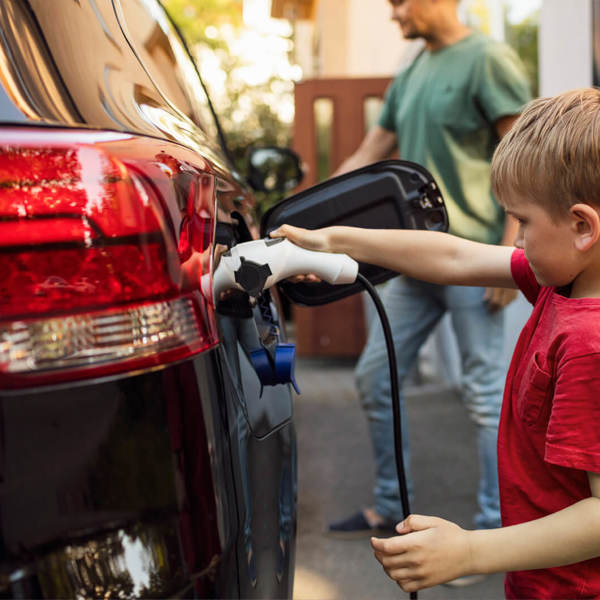 Child in red shirt plugs an electric vehicle charger into a car
